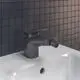 Schwarze Bidetarmatur von Ideal Standard mit einem schlichten Design und einem drehbaren Auslauf, montiert auf einem weißen Waschbecken vor einer gefliesten Wand.